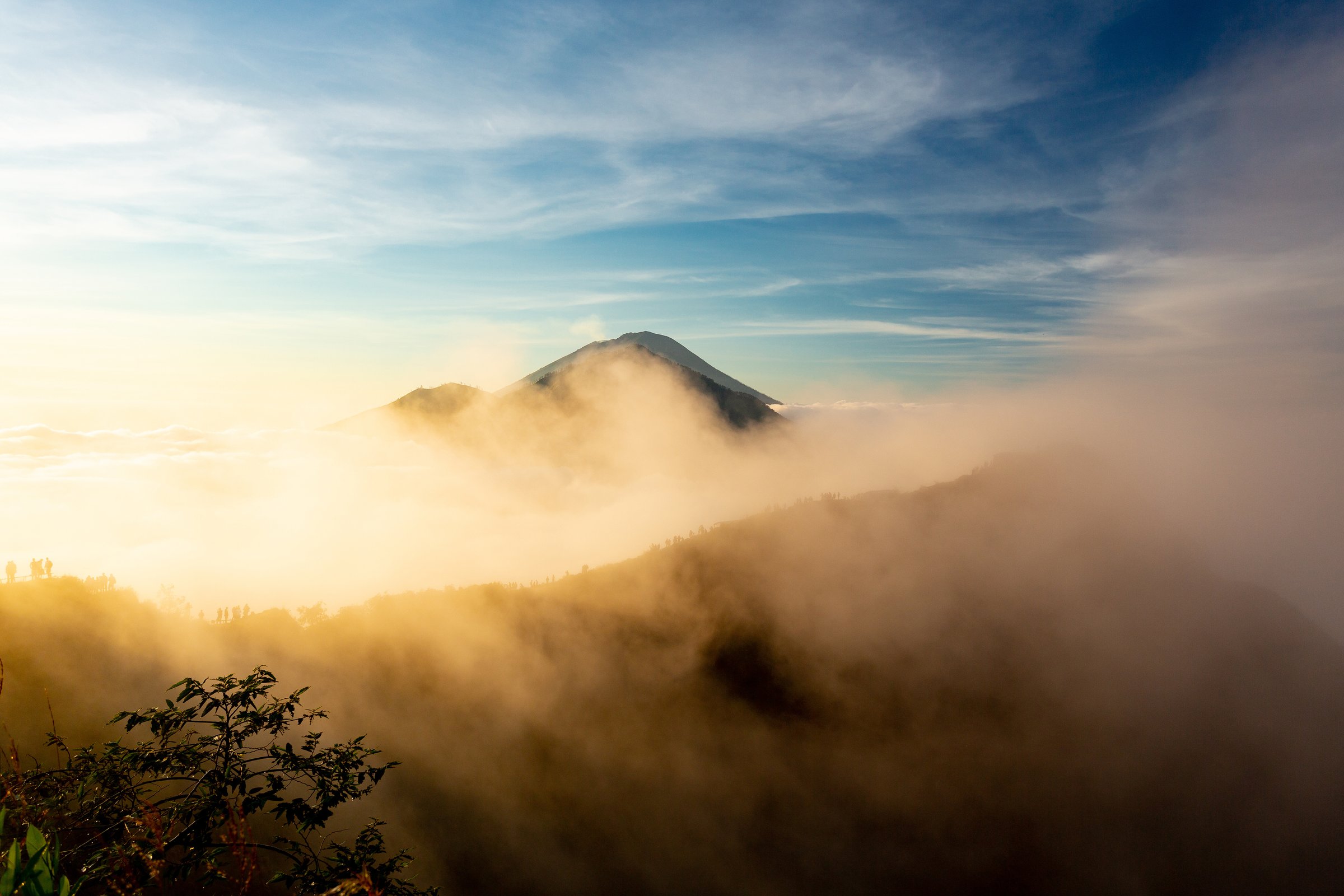 Mount Rinjani summit rising above golden morning mist and clouds at sunrise