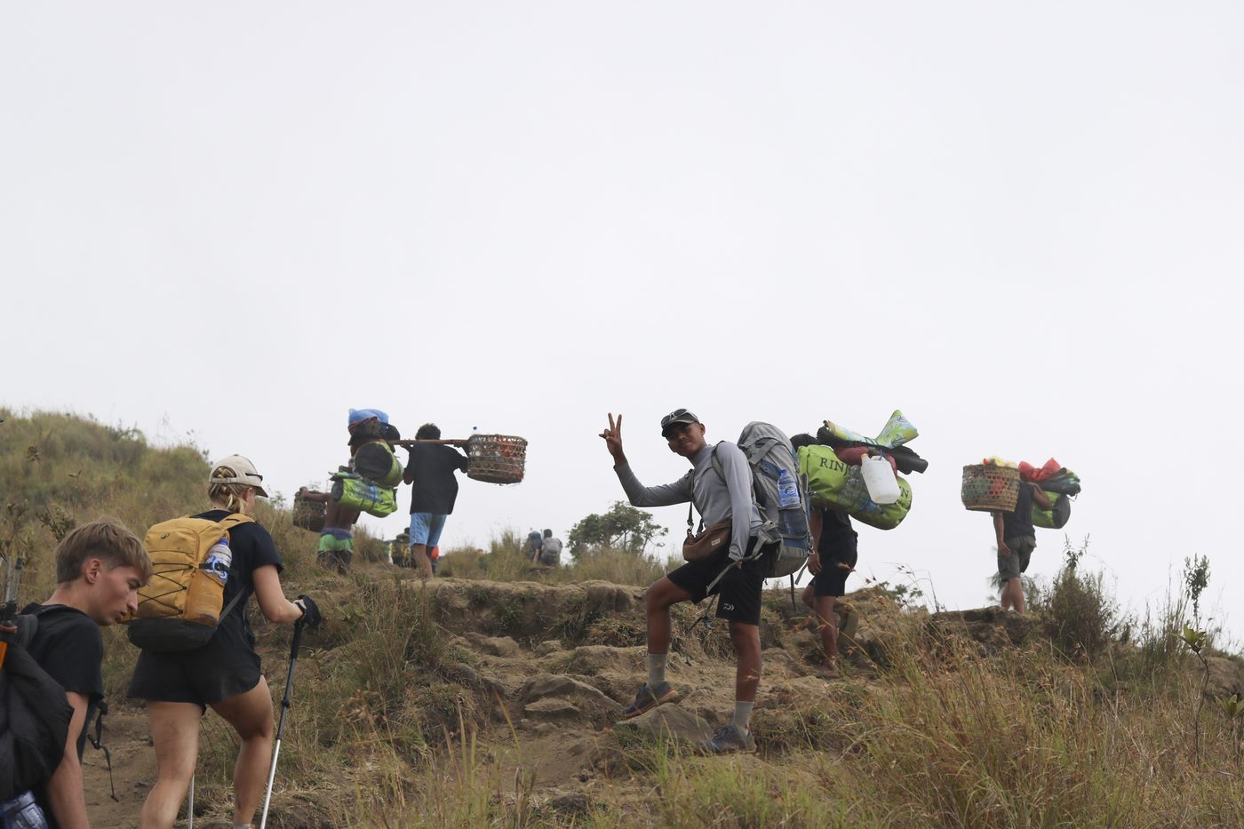 Porters climbing the trail with baskets of food and water on their shoulders, carrying the camp kitchen up the mountain
