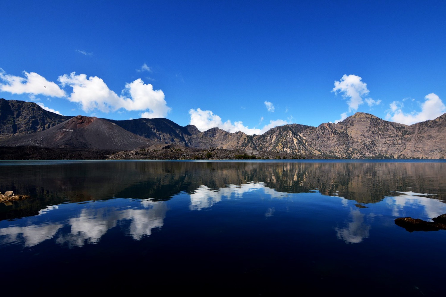 Segara Anak crater lake, still and blue, with the caldera walls reflected in it