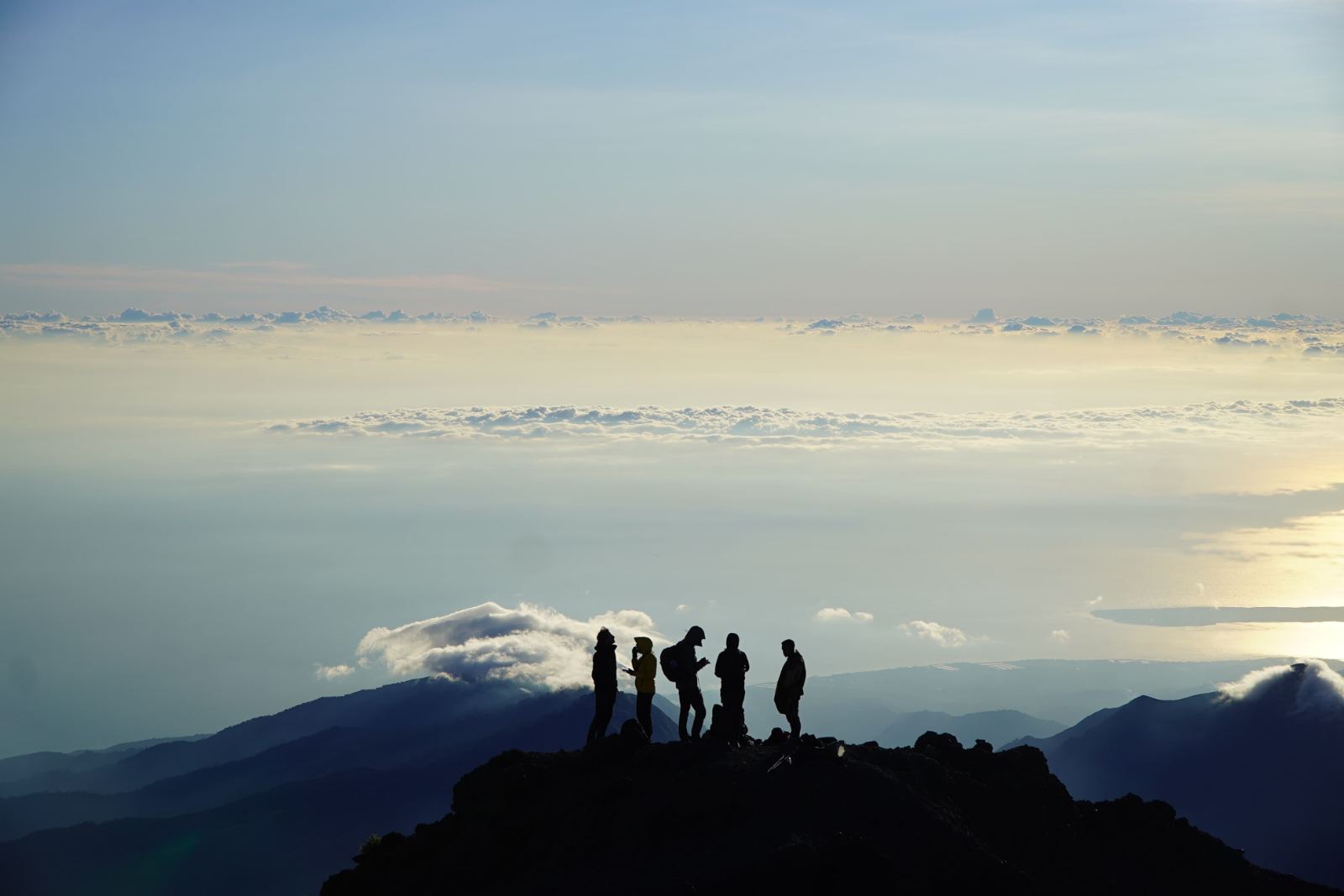 Trekkers silhouetted on a ridge above a sea of cloud at sunrise